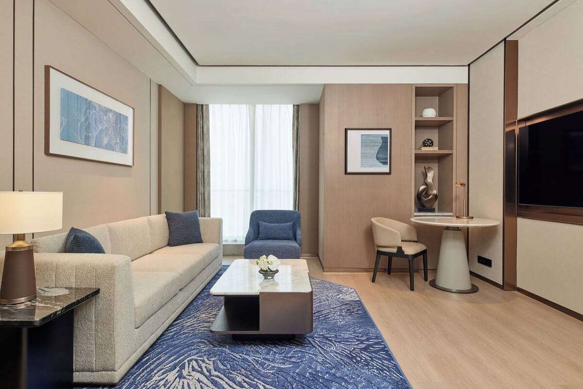 Une chambre d’hôtel moderne équipée d’un canapé, d’un fauteuil, d’une table basse, d’une télévision et d’un petit coin repas.