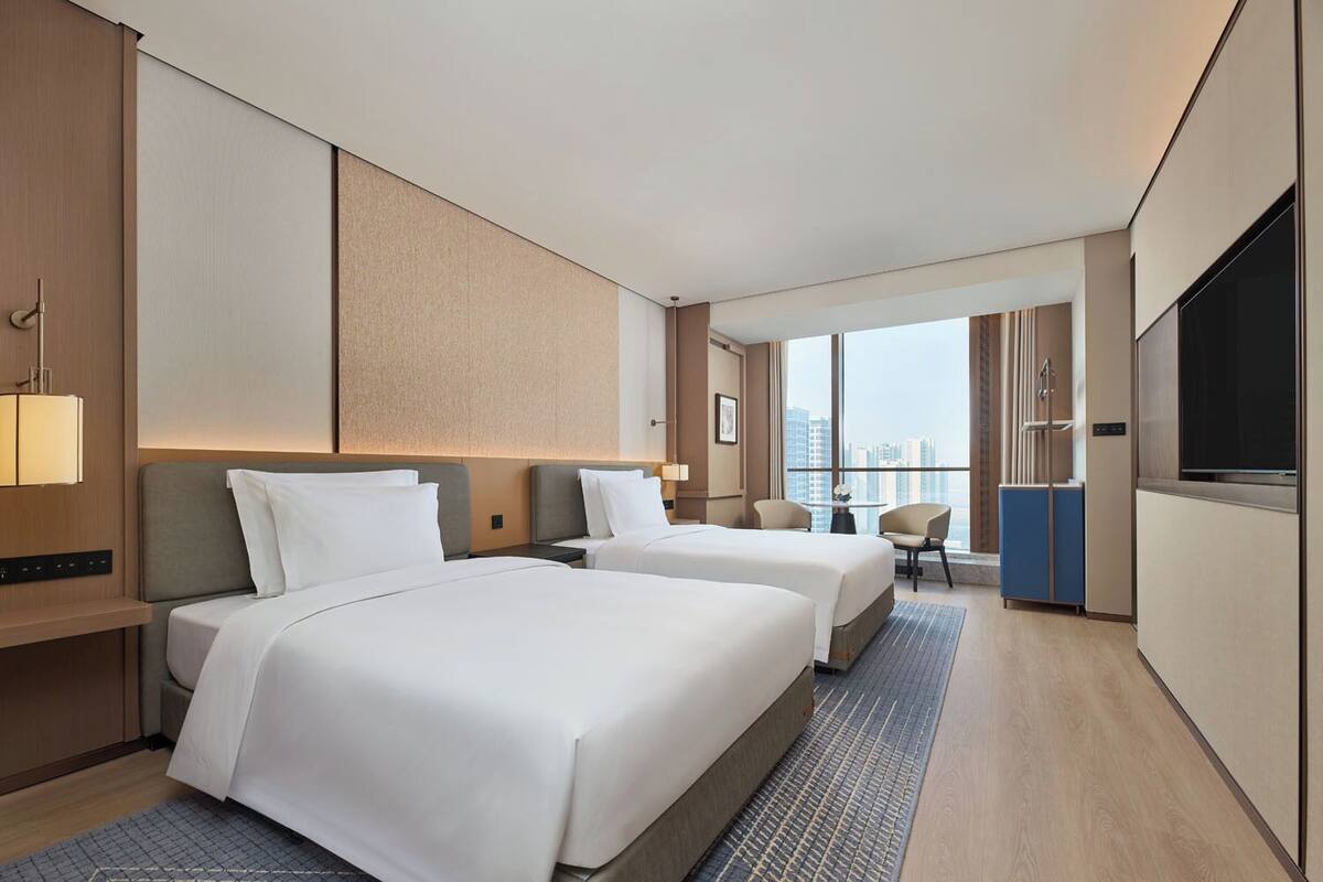 Une chambre d’hôtel avec deux lits, une télévision, un bureau et une vue sur la ville.
