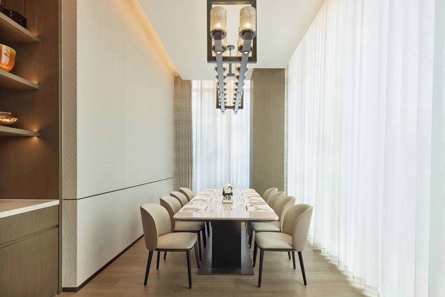 Une salle de conférence moderne, dotée d’une longue table, de chaises beiges et d’un lustre.