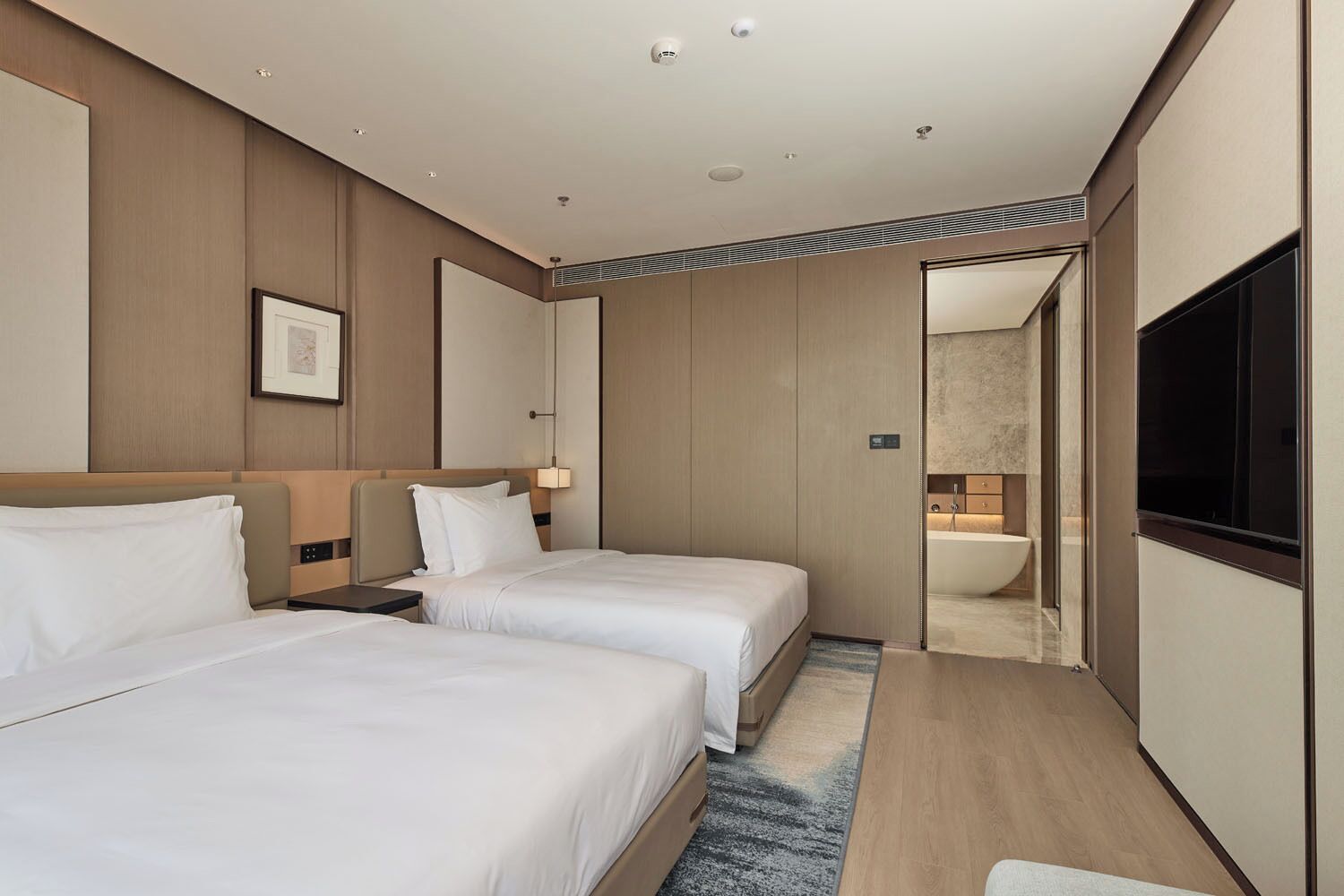 A hotel room with two beds, a large mirror, a flat-screen TV, and a bathroom visible through an open door.