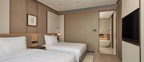 A hotel room with two beds, a large mirror, a flat-screen TV, and a bathroom visible through an open door.