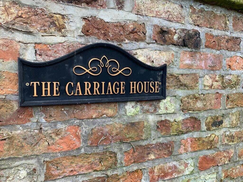 Un letrero negro con letras doradas en una pared de ladrillo que dice "THE CARRIAGE HOUSE".