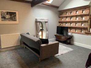 A cozy room with a sofa, a television, a radiator, and a brick wall shelf. - Studio 3B, The Carriage House. (Bilbrough)