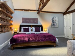 A bedroom with a wooden bed, a brick wall, a painting, and a door. - Studio 3B, The Carriage House. (Bilbrough)
