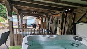 Un bain à remous installé sous une pergola en bois, avec vue sur un jardin et un espace de détente extérieur.