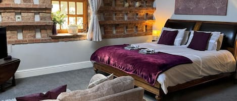 A bedroom with exposed wooden beams, a brick accent wall, a bed with a purple bedspread, and a window with curtains.