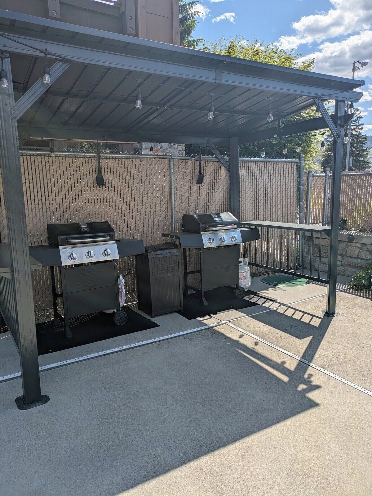 Zona de barbacoa al aire libre con dos parrillas y un área de estar techada.