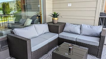 Un sofá seccional de mimbre con cojines grises en un patio al aire libre.