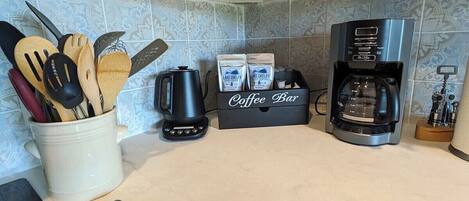 A kitchen with wooden cabinets, a coffee maker, a coffee bar, and a bottle of wine.