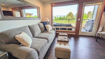 A living room with a sofa, ottoman, and a view through a glass door.