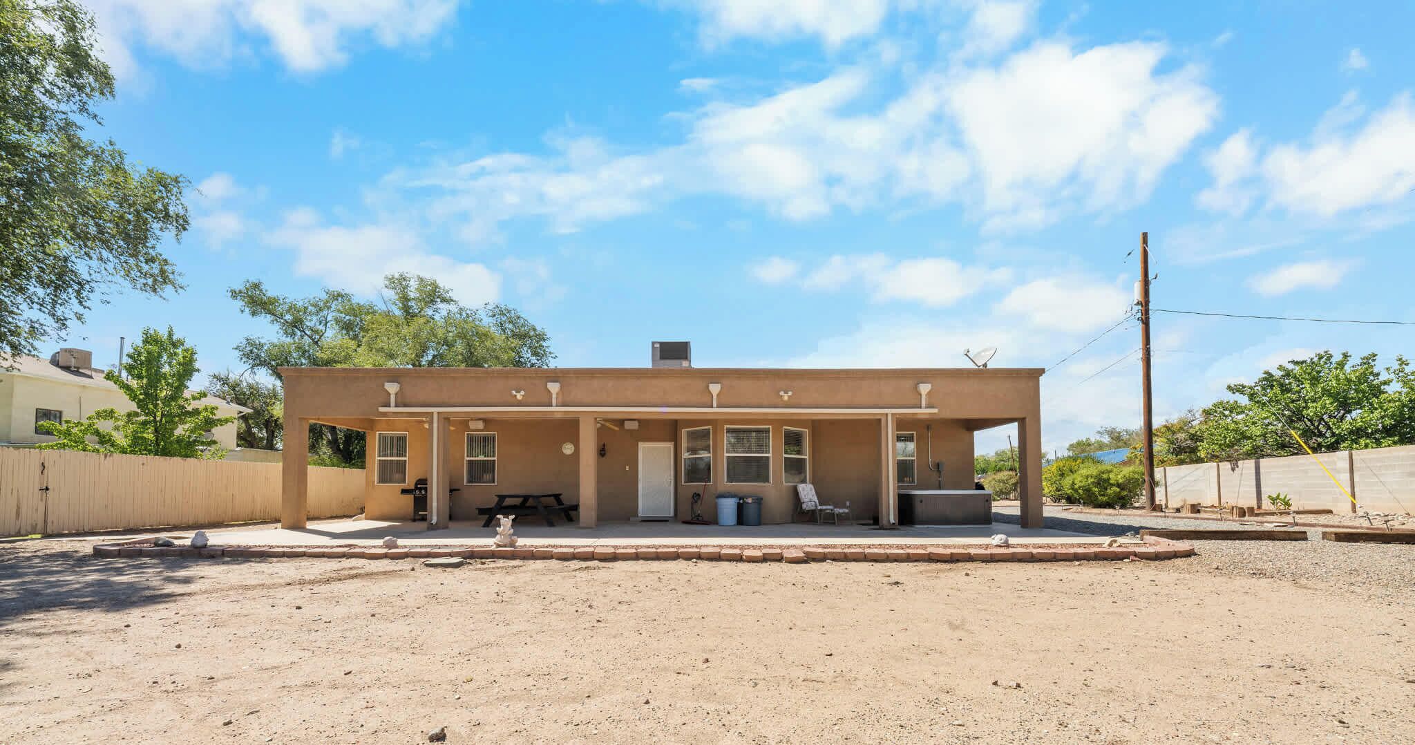 A single-story building with a covered patio area, a small attached structure, and a dirt ground.