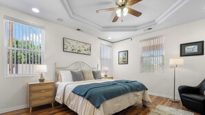 Ein Schlafzimmer mit Bett, Nachttischen, einem Deckenventilator und großen Fenstern.