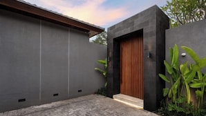 Un edificio moderno con fachada oscura, puerta de madera y un área de entrada empavedada.