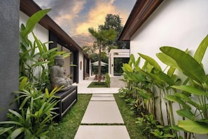A narrow pathway leading to a seating area with a Buddha statue, surrounded by lush greenery and a clear sky. - Villa Cocktail and Dreams by BaliSuperHost (Bali)