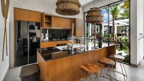 Una cocina moderna con una isla central, armarios de madera y un amplio ventanal con vistas a la vegetación.