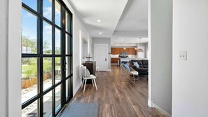 A spacious hallway with a large glass door leading to an outdoor area, a kitchen with wooden cabinets, and a seating area with a sofa and chairs. - Tiger's Cove - Hot Tub, Boat Lift, & Fire Pit! (Marble Falls)
