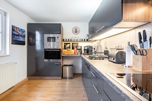 A modern kitchen with stainless steel appliances, a wooden floor, and a clock on the wall.