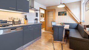 Een moderne keuken met grijze kastjes, een inbouw vaatwasser en een houten eethoek met een bank.