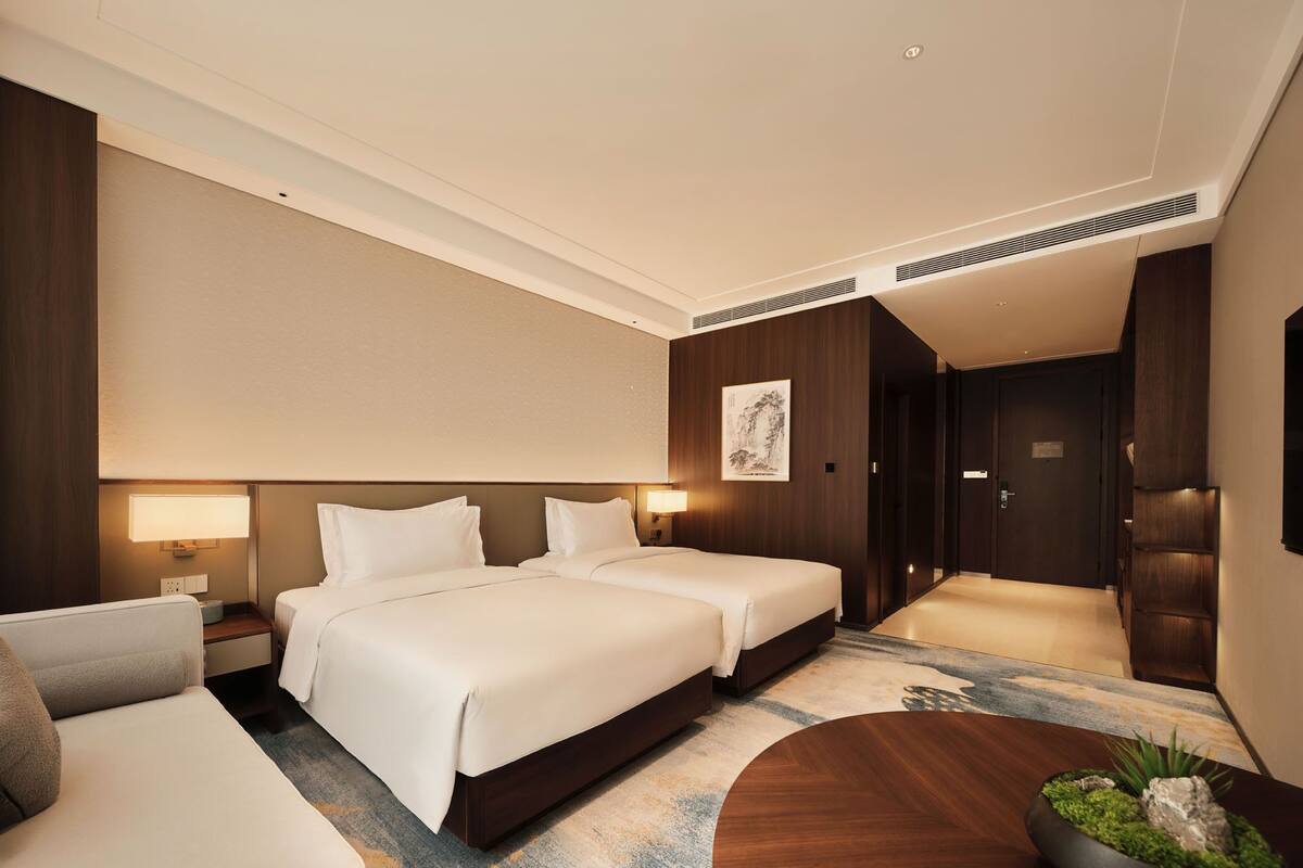 Habitación de hotel con dos camas, un sofá, una mesita y un cuadro en la pared.