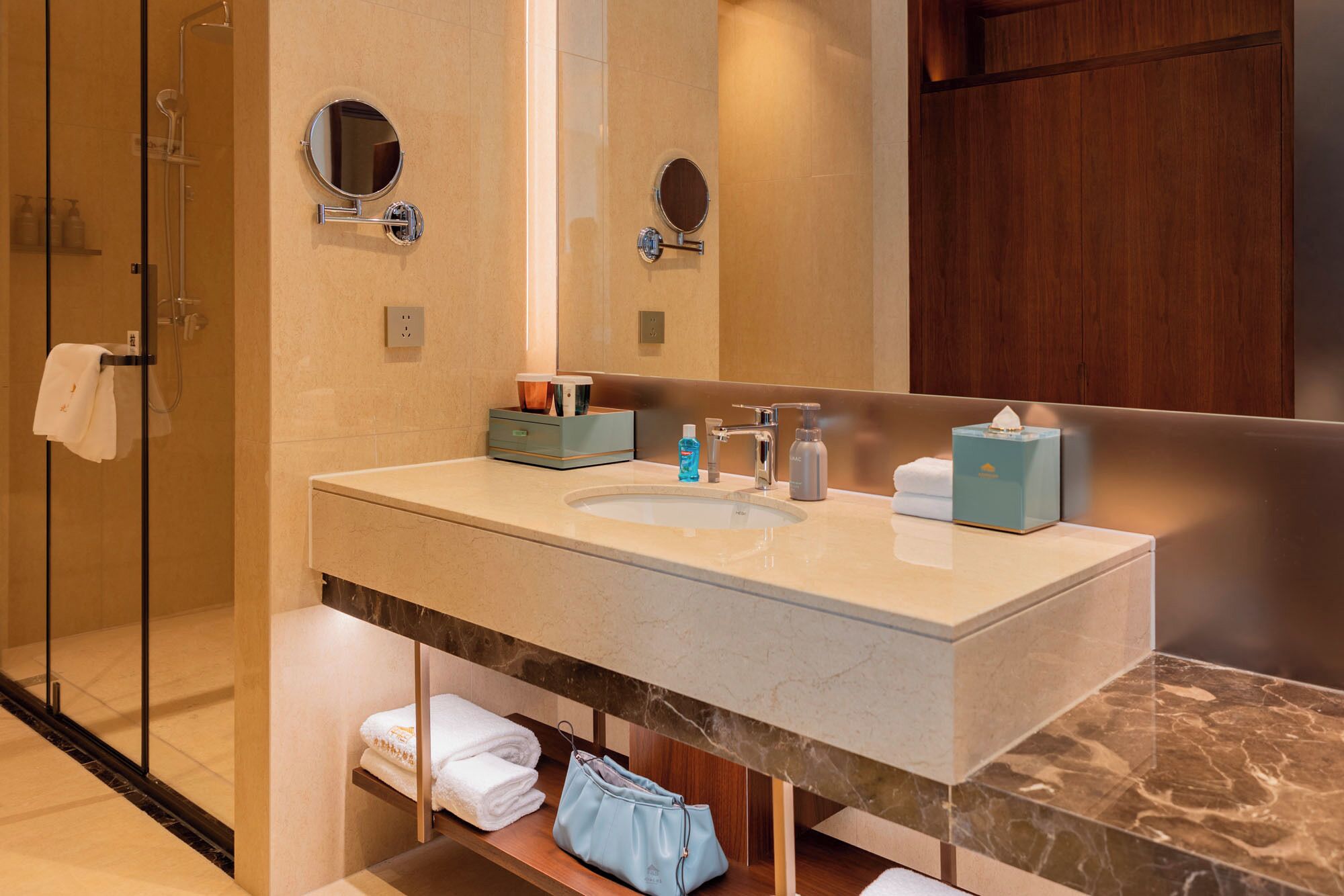 Un bagno con box doccia in vetro, lavabo con piano in marmo e specchio sopra il lavabo.