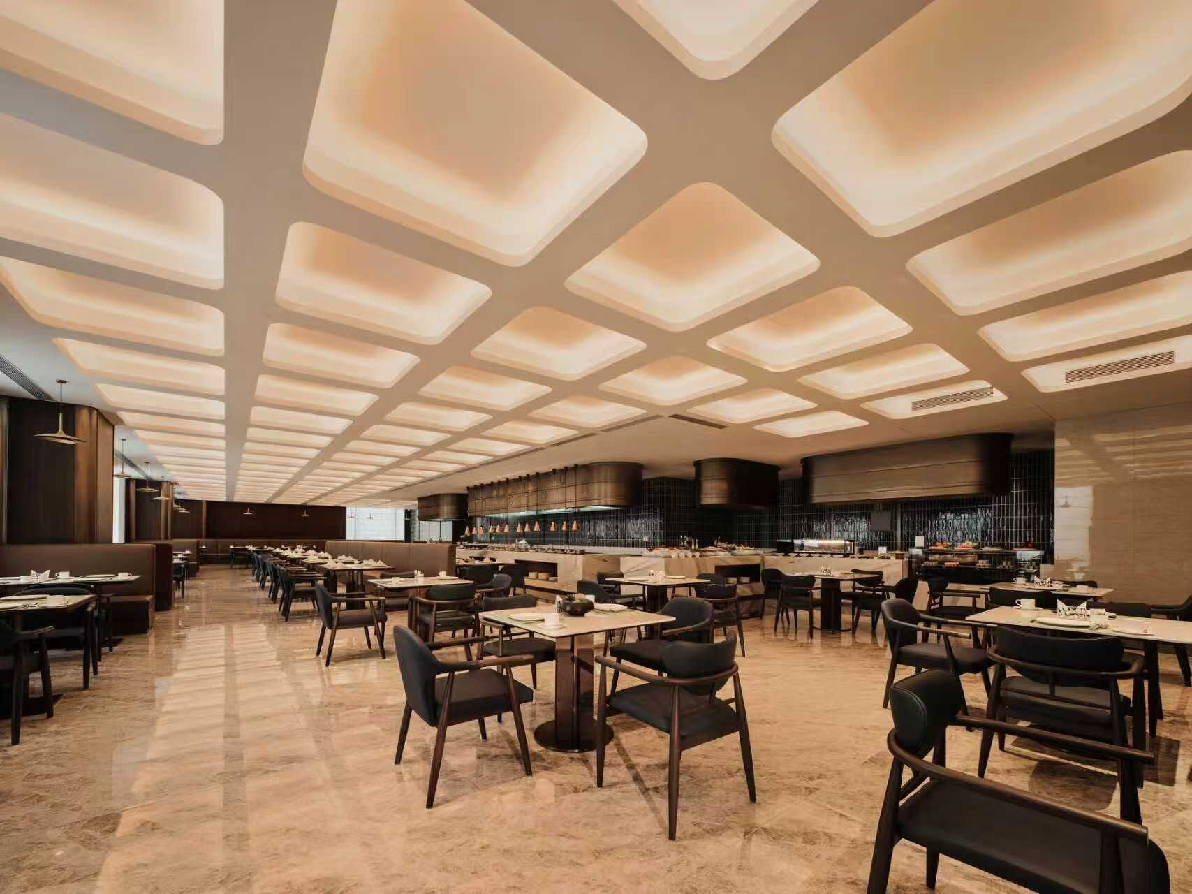 A spacious restaurant with a modern ceiling design, multiple dining tables, and a long counter.