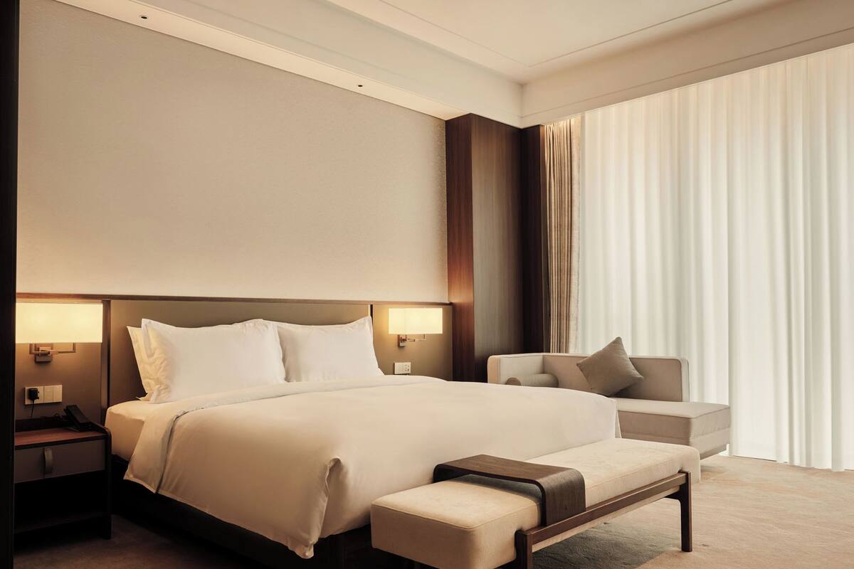Una habitación de hotel con una cama grande, lámparas de noche, un sofá y un banco.