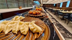 Un buffet proposant une variété de plats, notamment des raviolis et des pâtisseries, dans un espace de restauration moderne doté d’un long comptoir et de sièges situés à droite.
