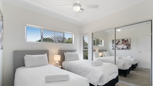 A hotel room with two beds, a ceiling fan, a large mirror, and a window with a view of trees. - Family-Friendly House with Courtyard Retreat (Wavell Heights)