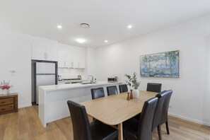 Une cuisine moderne avec des meubles blancs, un îlot central et un coin repas comprenant une table en bois et des chaises noires.