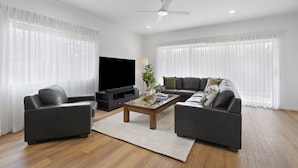 A modern living room with a flat-screen TV, two sofas, a coffee table, and a ceiling fan. - Family-Friendly House with Courtyard Retreat (Wavell Heights)