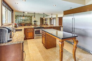 A spacious kitchen with granite countertops, wooden cabinets, a stainless steel refrigerator, and a large island. - Golf, Swim & Grill: Snowbird’s Escape in Sun Lakes (Sun Lakes)