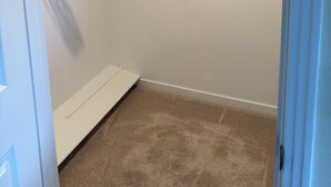 Ein begehbarer Kleiderschrank mit einer Holzbalkenablage, weißen Kleiderbügeln und einem beigefarbenen Teppich.