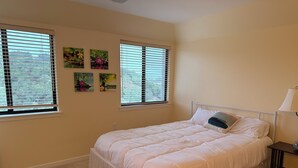 Ein Schlafzimmer mit einem großen Bett, zwei Fenstern mit Jalousien und Wandbildern.