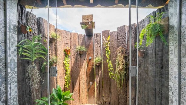 A glass-enclosed patio with a rustic wooden wall, potted plants, and a tiled floor.