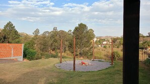 A circular gravel area with a statue, surrounded by grass and trees, with a brick wall and wooden posts in the foreground.