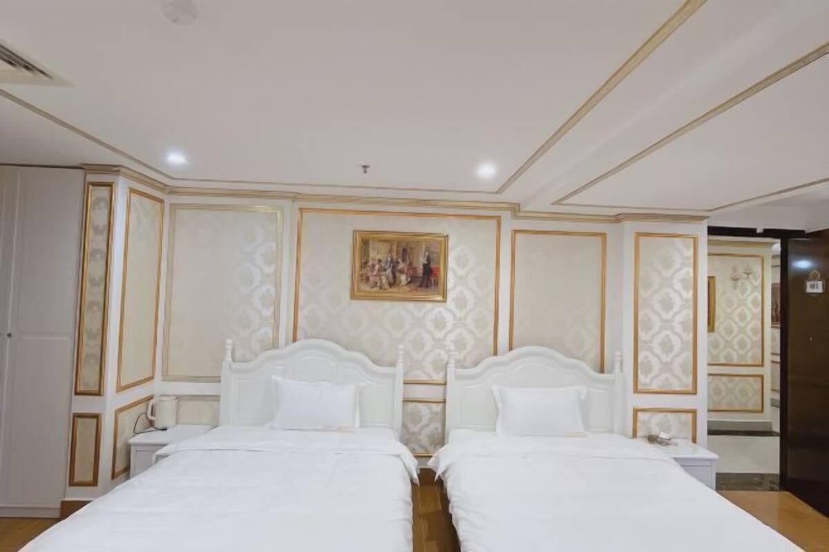 A hotel room with two beds, a painting on the wall, and a door to the right.
