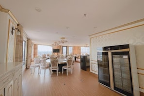 A spacious kitchen with a dining area, featuring a large refrigerator, a chandelier, and a view through the window. - KIM A HOTEL (Bac Ninh)