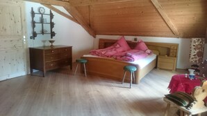 Een slaapkamer met een houten plafond, een bed met roze geruit beddengoed, een houten dressoir en een stoel.