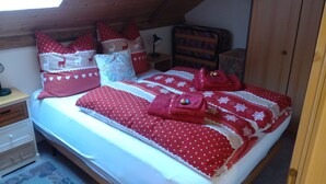 Een slaapkamer met een schuine kap, houten wanden en een bed met rode en witte beddengoed.