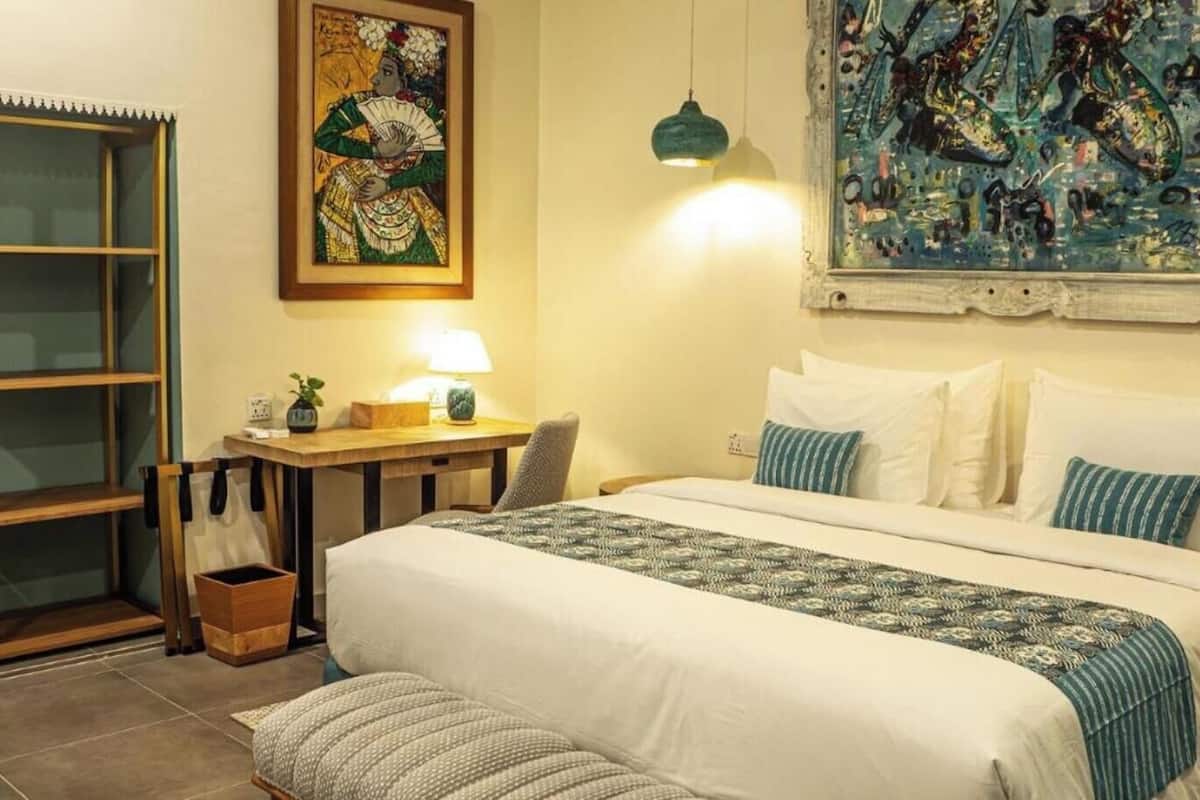 Un dormitorio con cama, mesita de noche, lámpara y una obra de arte en la pared.