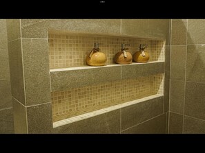 A bathroom with a tiled wall, a shelf with three bottles, and a lower shelf with a tiled design. - Roka Resort by ARKasia Foundation (Bintan)