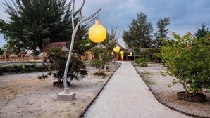 A pathway lined with trees and a row of yellow spherical lights leading to a building with a red roof. - Roka Resort by ARKasia Foundation (Bintan)
