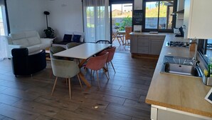 A modern kitchen with a dining area, featuring a wooden table, chairs, and a sofa. - Les trois songes Villa where partying is tolerated in the countryside  (Saint-Pierre)