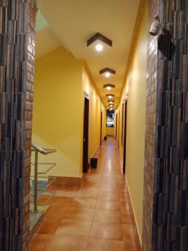 A long, narrow hallway with yellow walls and a tiled floor, leading to a door at the end. - Sahoo Palace (Brahmagiri)