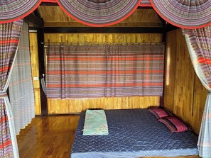 Ein kleiner, gemütlicher Raum mit einem Bett, einer Holzbalkendecke und gemusterten Vorhängen.