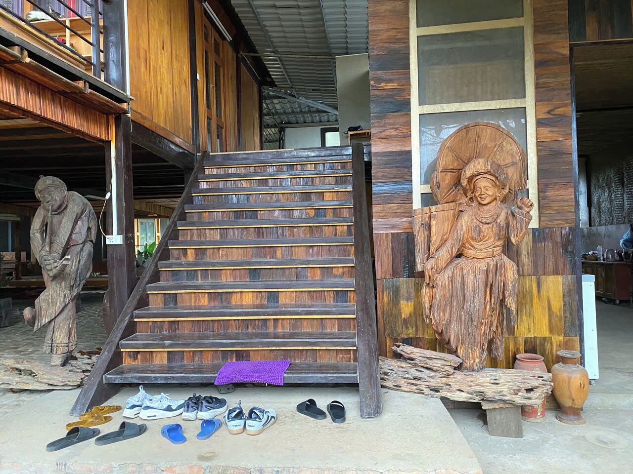 A wooden staircase leading to a building with a large wooden sculpture on the right.