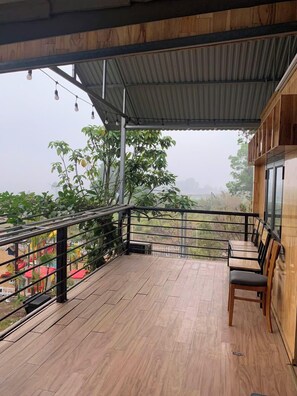 Eine Holzterrasse mit Metallgeländer, einem Tisch mit Stühlen und Blick auf Grünflächen und Gebäude in der Ferne.