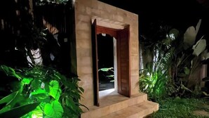 Une petite construction moderne, dotée d’une porte en bois et de quelques marches, entourée d’une végétation luxuriante.