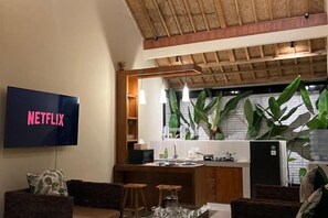 A living room with a television displaying "NETFLIX," a kitchen area with a refrigerator, and a dining area with stools. - SEAOM Villas (Bali)