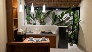 Une cuisine compacte dotée d’un îlot central, de luminaires suspendus et de grandes plantes vertes.